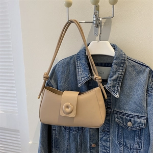 Detail of beige minimalist baguette bag with knot strap and circular decorative buckle