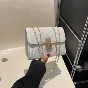 White quilted chain shoulder bag with gold clasp held by a model in a minimalist setting
