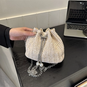 Sac seau en paille avec chaîne argentée et détails en perles sur bureau noir