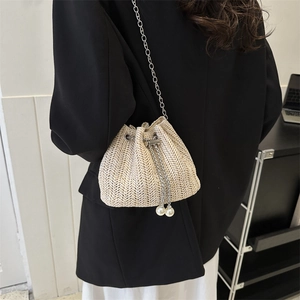 Sac seau en paille beige avec chaîne argentée et perles porté par un modèle