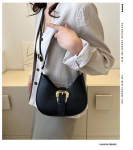 Detail of black croc-embossed saddle bag with gold baroque buckle on model's shoulder