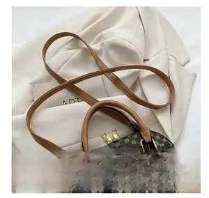 Detailweergave van bruine monogram schelptas met gouden ritsen en leren riem