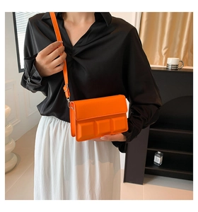 Detail of bright orange chocolate cube crossbody bag worn with a black shirt and white skirt