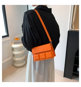 Detail view of bright orange crossbody bag with 3D chocolate grid texture on a model