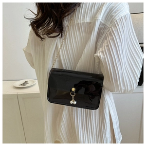 Détail du sac bandoulière en cuir verni noir avec chaîne dorée et perles sur un modèle