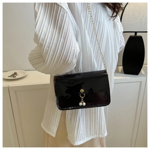 Détail d'un sac bandoulière en cuir verni noir avec chaîne dorée et pendentifs en perles