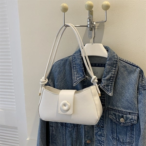 Detail of white minimalist underarm bag featuring a 3D floral clasp and knotted strap