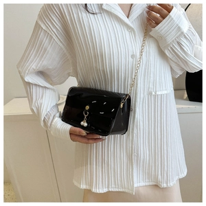 Détail d'un sac en PVC noir brillant avec perles porté sur une chemise rayée