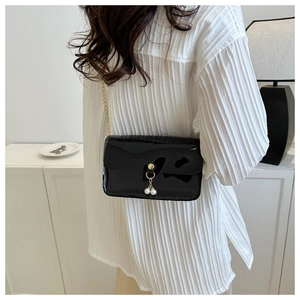 Détail d'un sac bandoulière en cuir verni noir avec breloque perle et chaîne dorée
