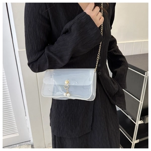 Détail du sac transparent en PVC avec chaîne dorée et élégants pendentifs en perles