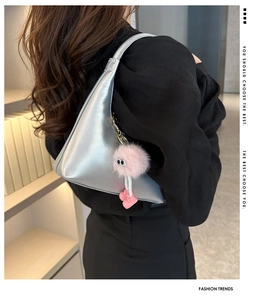 Detail of silver geometric underarm bag with a pink plush monster charm and marketing text