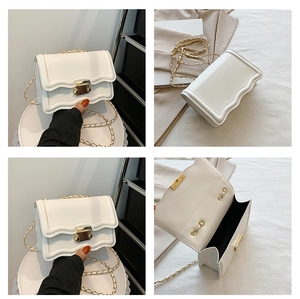 Detail view of white crossbody bag with scalloped edges and gold chain strap and lock