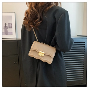 Detail of scalloped edge beige crossbody bag with gold chain and metal buckle