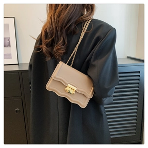 Detail of khaki leather shoulder bag with scalloped flap and gold metal clasp on a model