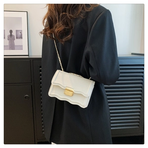 Close-up of white crossbody bag with wavy edges and gold chain strap on a black suit