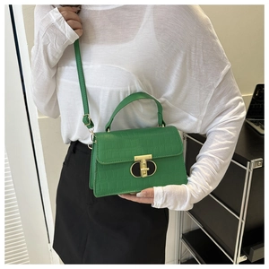 Detailed view of green crocodile pattern handbag with gold T-bar lock on a shoulder strap
