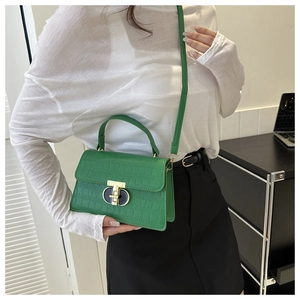 Detail of green crocodile pattern handbag featuring a gold twist lock and adjustable strap