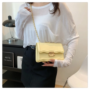 Detail of light beige crossbody bag with scalloped edges and gold buckle on a model