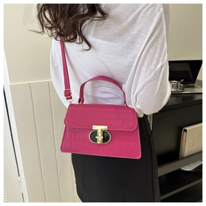 Detail of hot pink crocodile pattern handbag with golden T-lock and adjustable strap