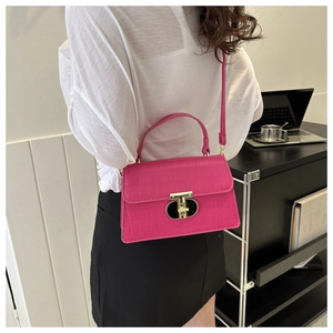 Detail of rose pink crocodile embossed handbag featuring a gold T-shaped lock and handle