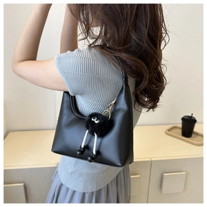 Close-up of black leather half-moon shoulder bag with a plush monster charm detail