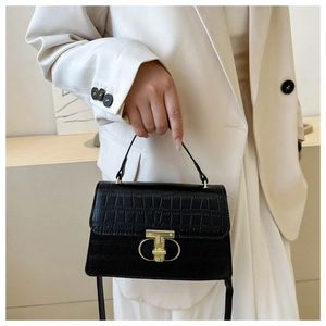 Detail of black crocodile embossed handbag with gold metal lock on a beige suit