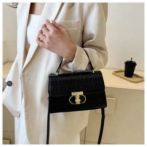 Close-up of black crocodile pattern handbag with gold clasp on a cream blazer