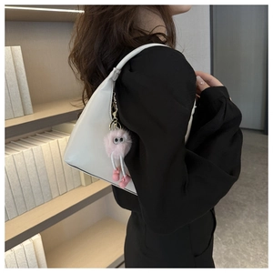 Minimalist white leather underarm bag with a cute pink plush monster charm detail
