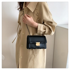 Detail of black crossbody bag with scalloped flap edge and gold rectangular buckle