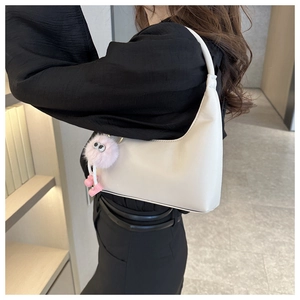 White minimalist hobo bag with a pink plush charm shown in a stylish shoulder carrying view