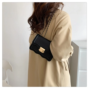 Detail of black crossbody bag with scalloped edge and golden twist lock on khaki trench coat