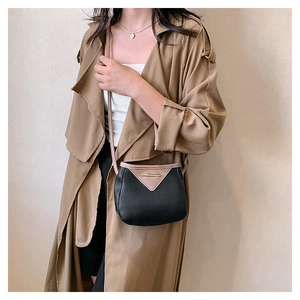 Sac bandoulière texture galet avec rabat en V contrasté porté sur un manteau de couleur kaki