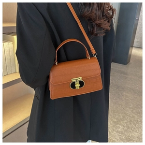 Detail of orange crocodile pattern leather handbag with gold T-shaped clasp on a blazer