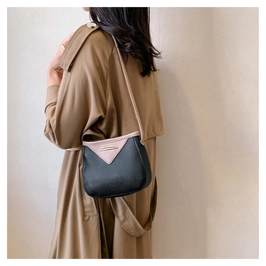 Detail view of pink and black contrast leather crossbody bag on model in a trench coat