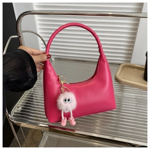 Detail of rose red leather crescent bag with a cute pink plush charm on metal shelf