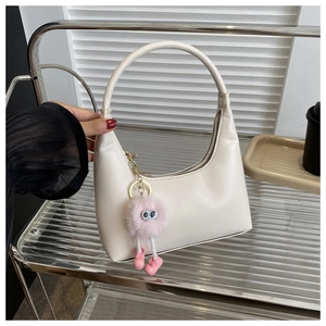 Detail of cream white underarm bag with cute pink plush monster charm on a shelf