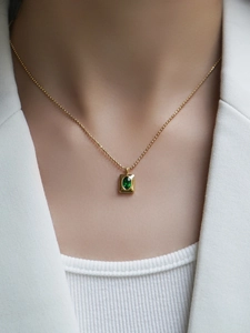 Collier élégant à boules dorées avec pendentif en zircon vert porté par un mannequin