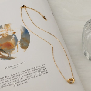 Minimalist knot pendant 18K gold plated titanium necklace on elegant magazine backdrop