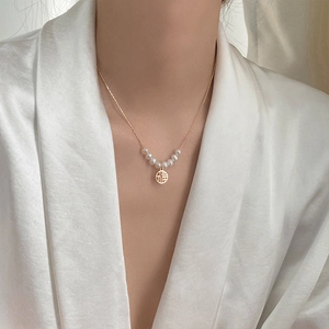Elegant gold pearl necklace with a Fu character pendant shown on a model's neck