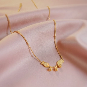 Elegant gold fish pendant necklace with round beads on silk fabric background