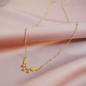 Minimalist gold necklace with fish and bead pendants on pink silk fabric background