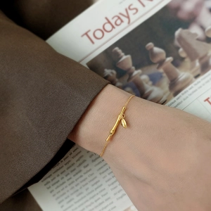Elegante bracciale dorato a forma di bambù con ciondolo a foglia indossato al polso
