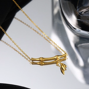 Collana minimalista in bambù dorato con piccoli ciondoli a foglia su superficie lucida