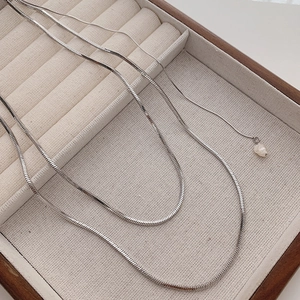 Minimalist silver snake chain necklace with a baroque pearl pendant on wooden tray