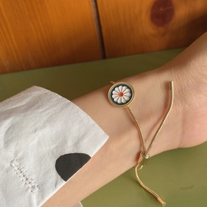 Adjustable golden snake chain bracelet with blue enamel daisy pendant on a wrist