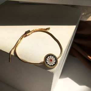 Adjustable gold snake chain bracelet with a blue enamel daisy pendant on white pedestal