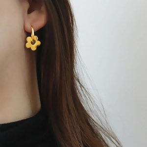 Boucles d'oreilles fleur en acier titane avec finition or mat portées par modèle