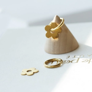 Boucles d'oreilles créoles fleurs dorées polies sur un support de cône en bois minimaliste