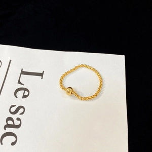 Minimalist gold chain ring with a polished metal bead on a white paper background