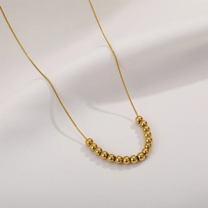 Minimalist 18K gold snake bone necklace with polished round beads on white fabric